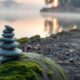 Misty lakeside path at dawn with balanced stone cairn representing overcoming negative self-talk
